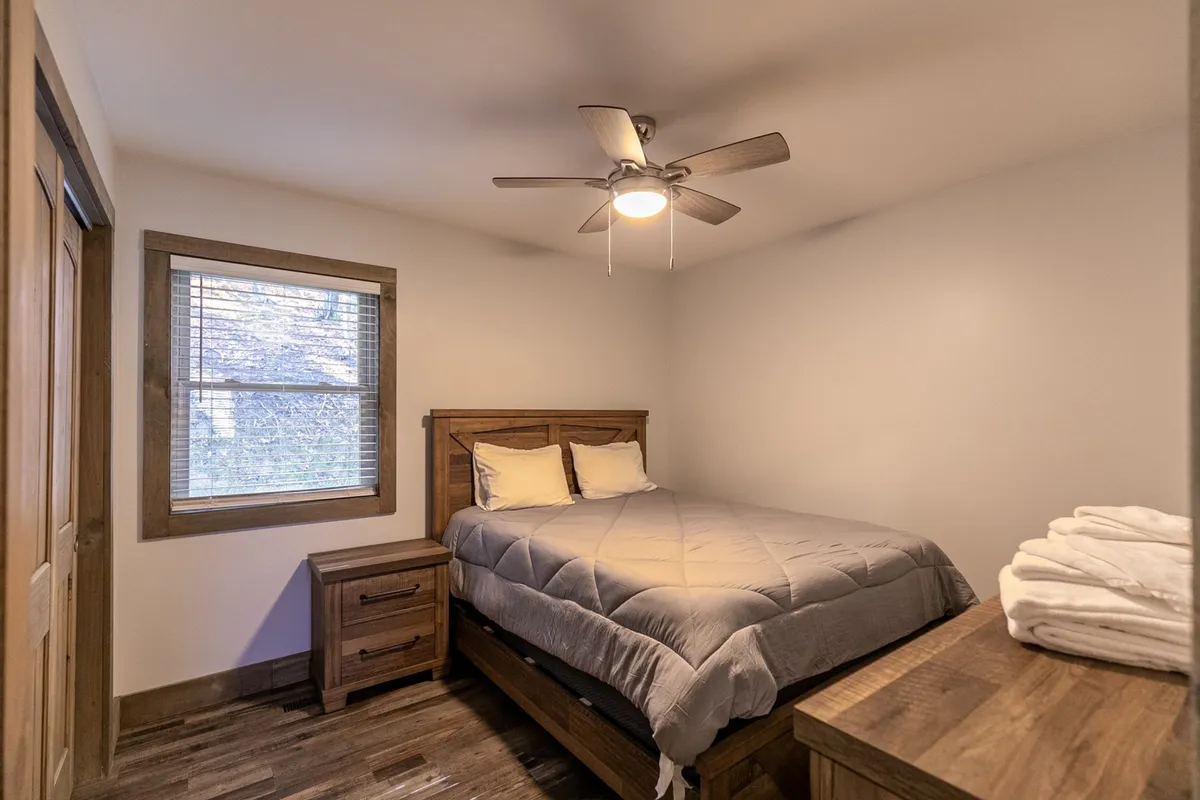 A cozy bedroom with a large bed dressed in luxurious linens, a nightstand beside it, and a window inviting soft natural light into the space. The serene mood promises relaxation and restful sleep.