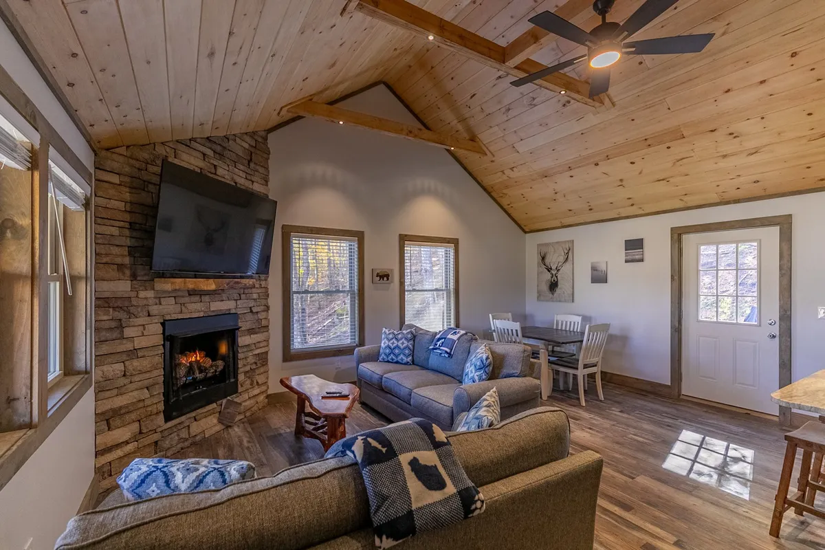 Another angle of the living and dining space, showing the inviting fireplace, comfortable sofa, dining table, and generous windows. The layout emphasizes how both spaces flow together, capturing the warmth and connection that define the central gathering area.