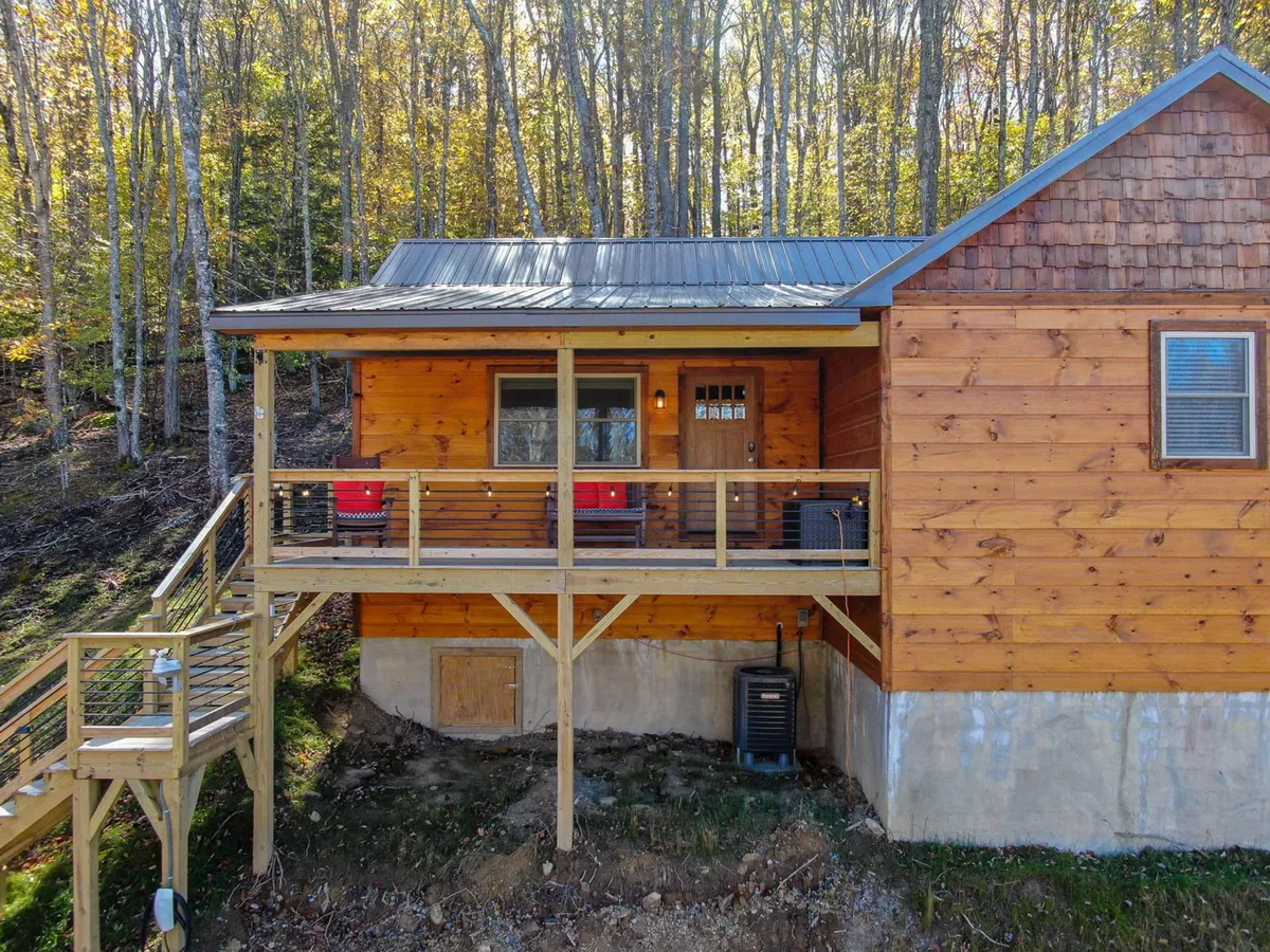 A cozy wooden porch with red chairs nestled amidst trees, showcasing the facade of the cabin. This spot offers views of the natural surroundings, providing a perfect space for gathering, sipping coffee, or stargazing after a day outdoors.