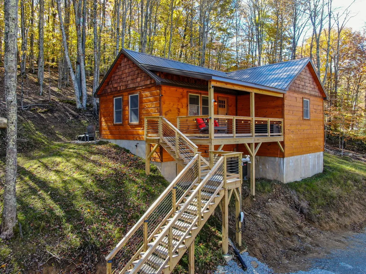 The image showcases the rustic wooden exterior of the Whiskey Rock cabin, highlighted by a welcoming front porch and a charming staircase leading up to the entrance. The cozy porch overlooks serene, wooded surroundings, inviting guests to relax and soak in mountain sunsets or gaze at the stars in the evening.