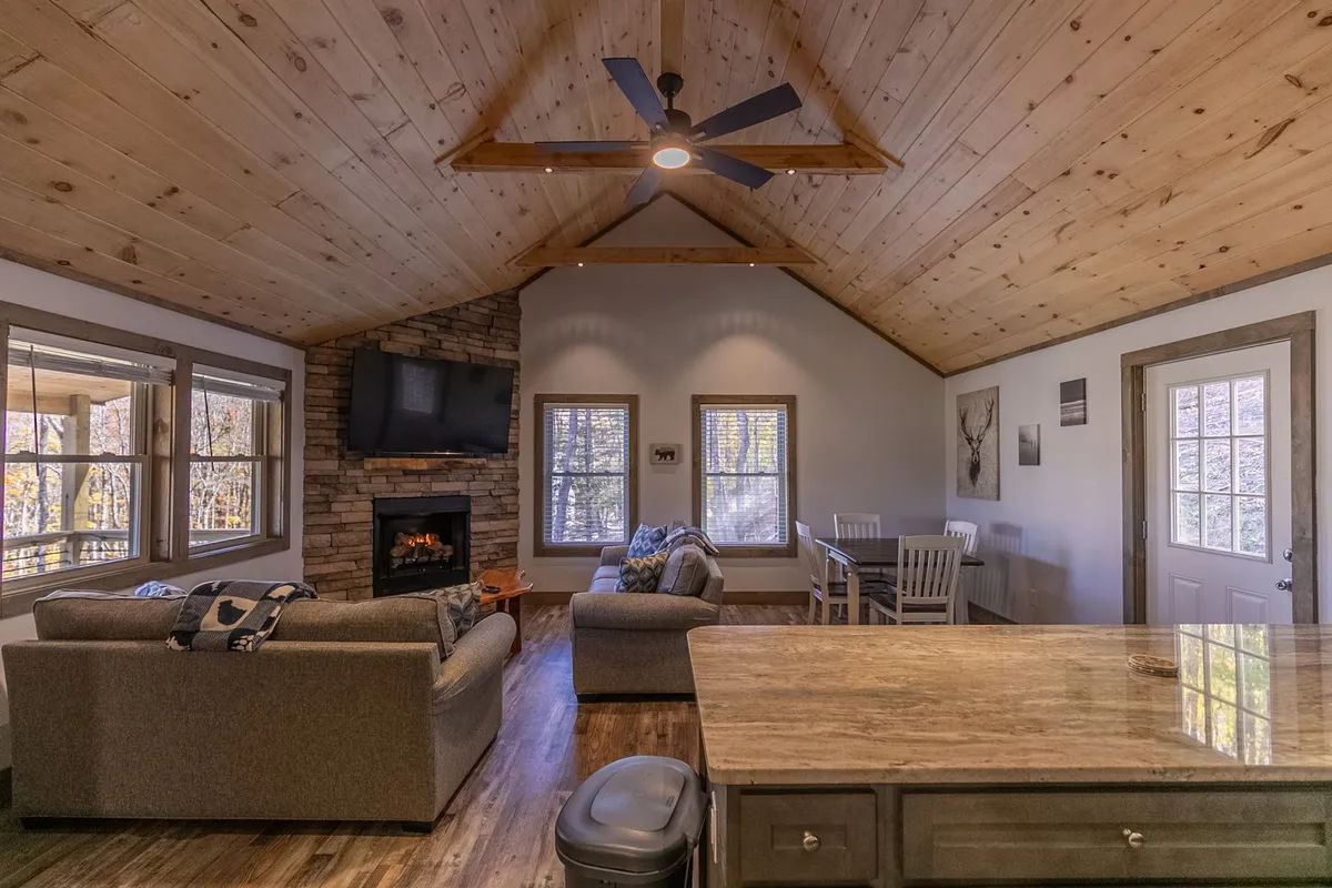 A cozy view into the living area, featuring a glowing fireplace, a welcoming seating arrangement, and a dining table. Sunlight streams in through the windows, illuminating the rustic details and making the space feel both intimate and open.