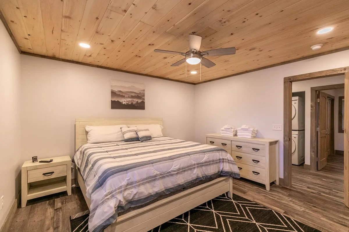 A calm and restful bedroom featuring a well-made bed, dresser, ceiling fan, and tasteful artwork. Soft daylight creates a soothing environment ideal for unwinding.